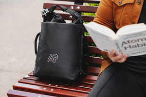 A man sitting on a bench reading a book with his travel backpack next to him. 