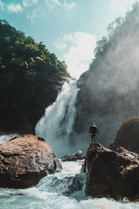 Man standing on a rock near a waterfall 